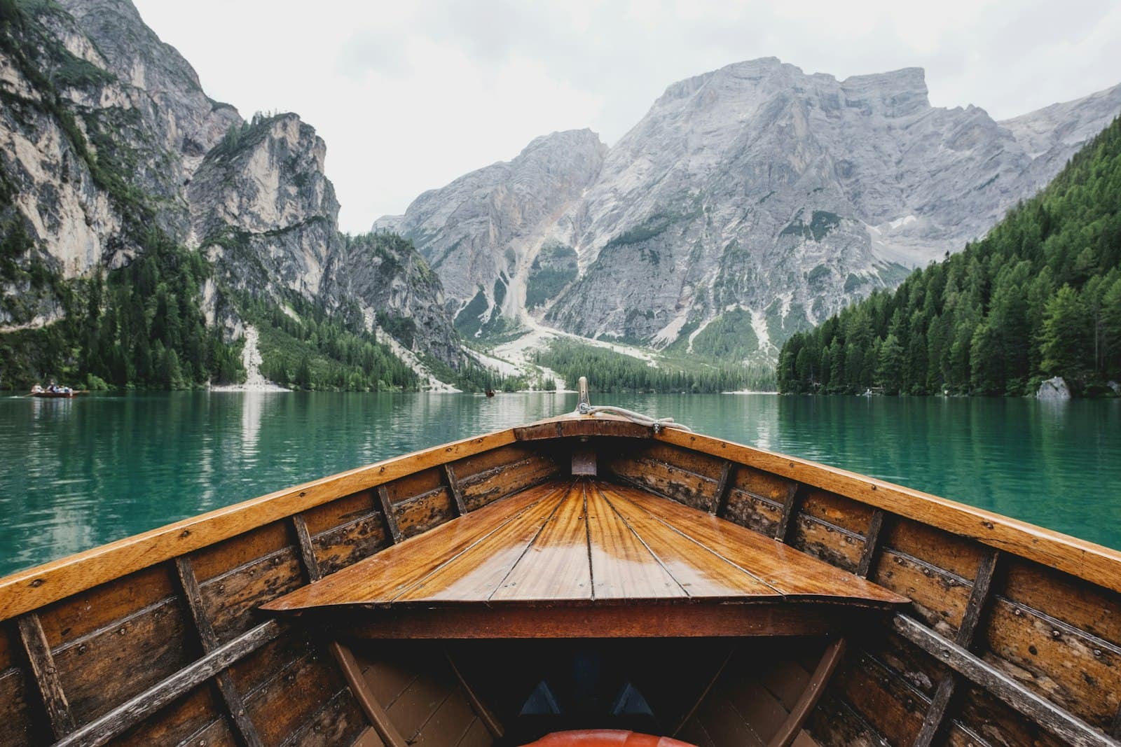 The bow of a wooden boat pointing across a still lake towards steep mountains