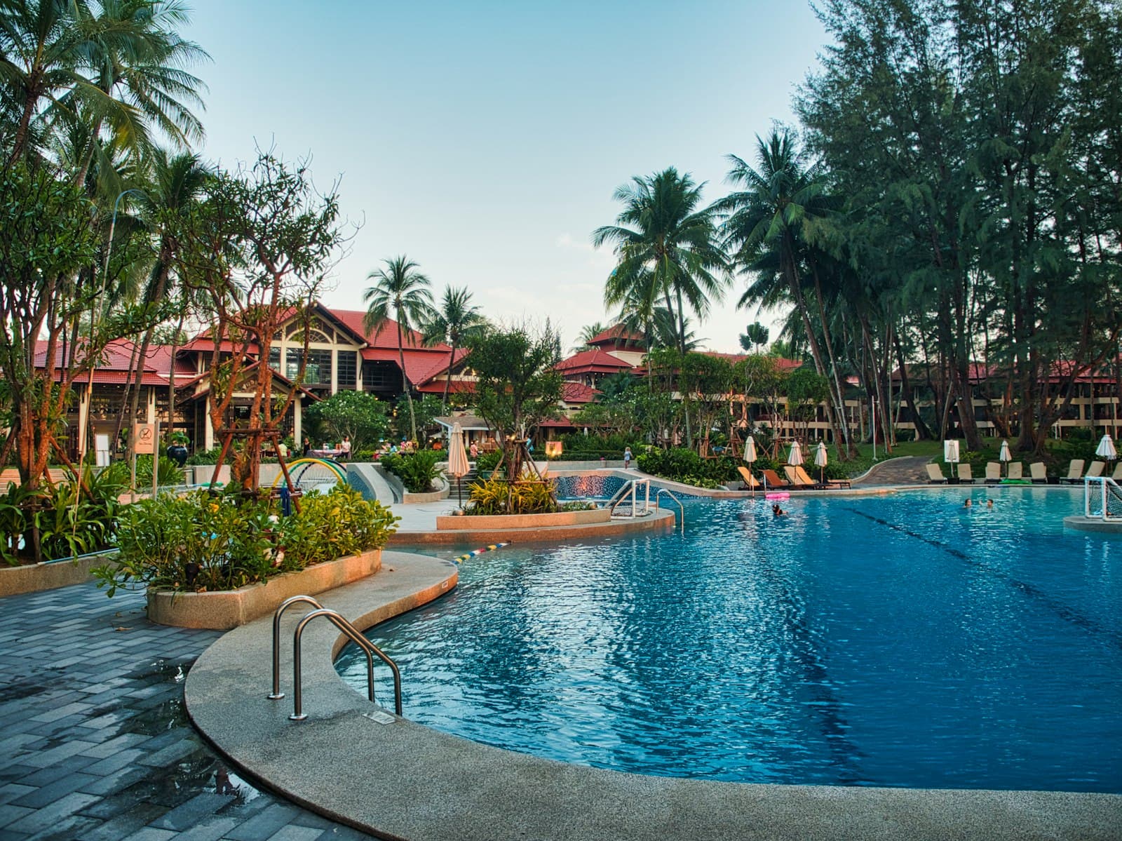 A tropical resort pool surrounded by palms and shaded loungers
